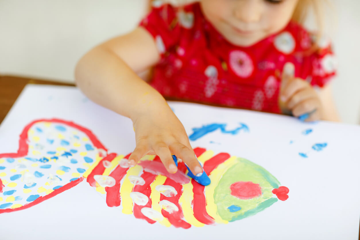 A toddler finger painting a fish.