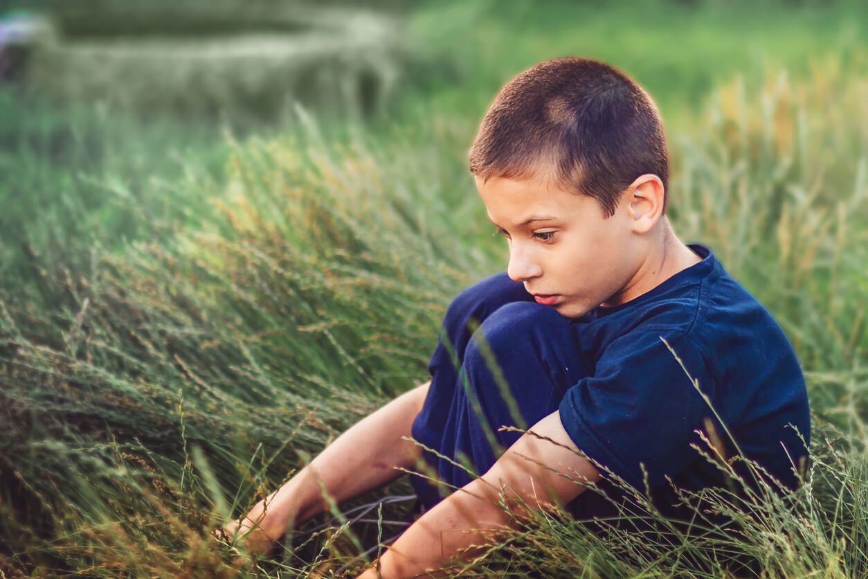 Un enfant assis dans l'herbe le regard dans le vide.