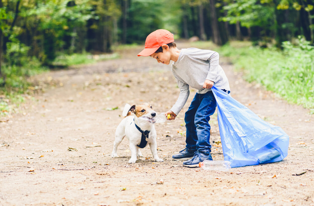 A child and his dog picking up garbage in the woods.