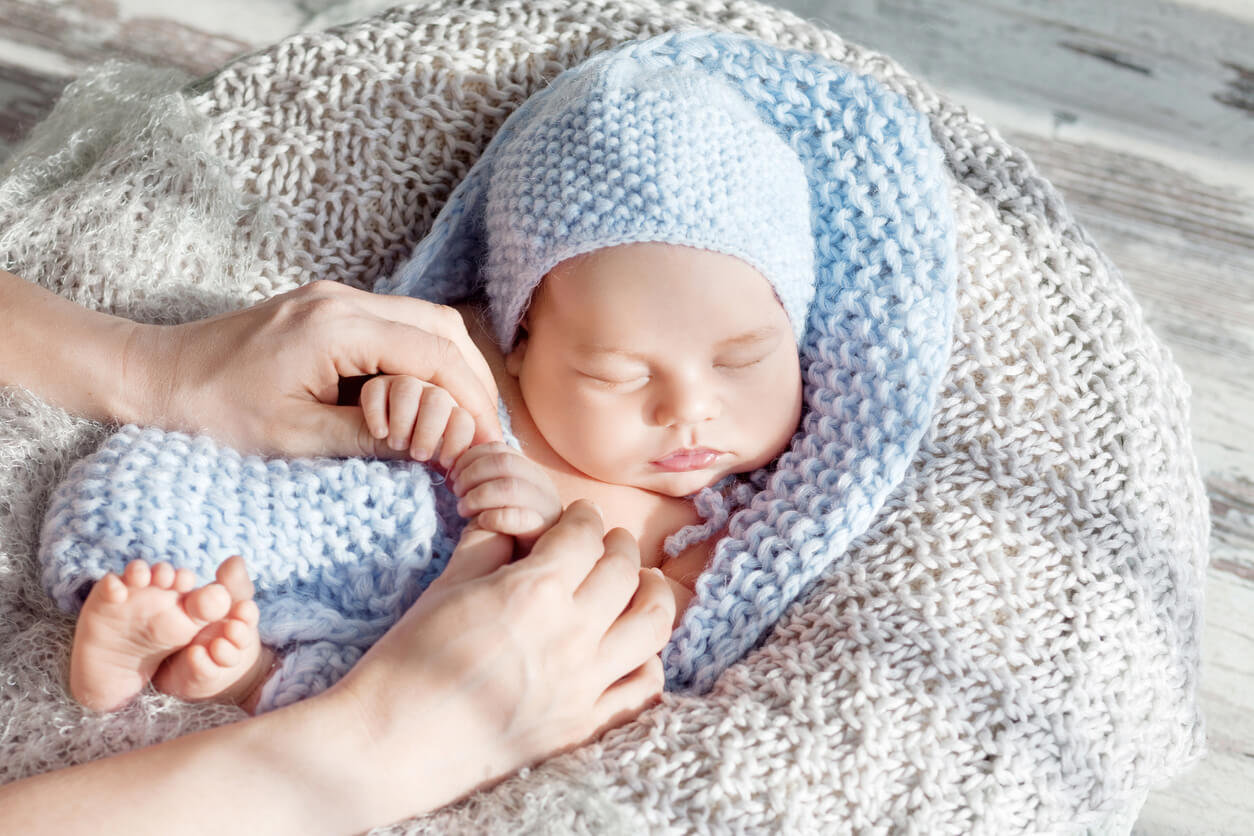 A person touching holding the hands of a newborn baby wrapped in a blue knit blanket.