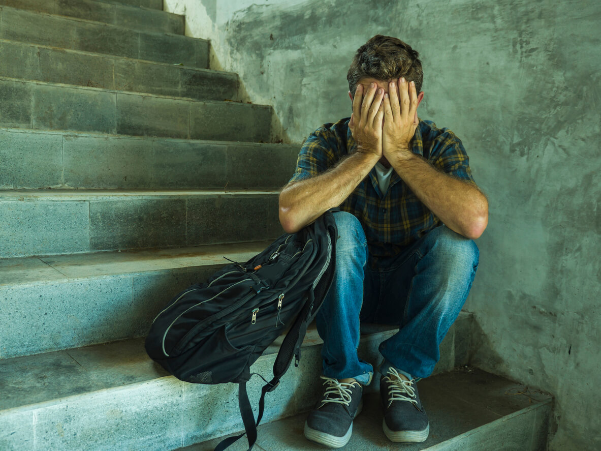 Un jeune homme le visage dans les mains assis dans un escalier.
