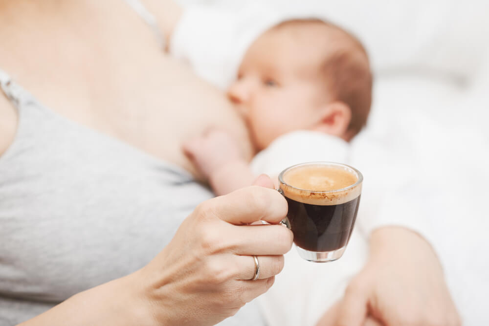 En mamma som dricker kaffe medan hon ammar.
