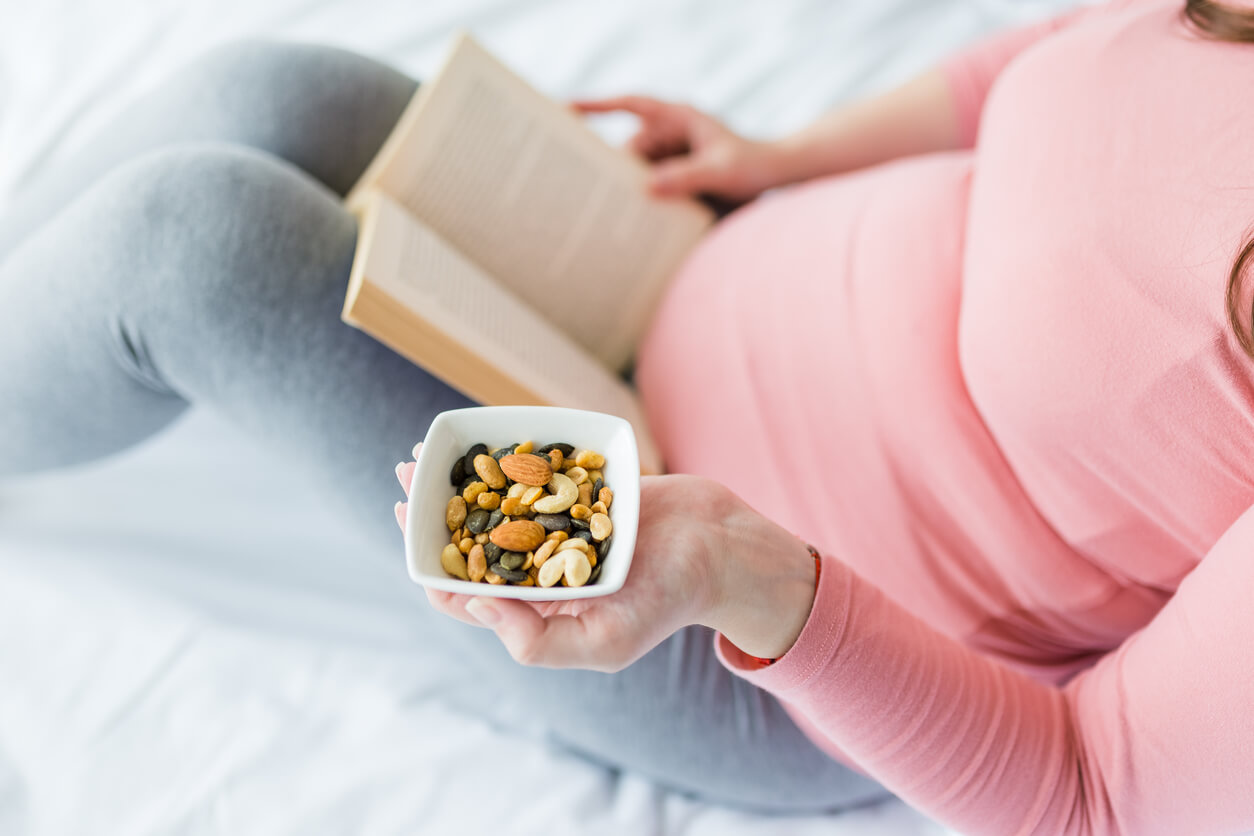 A pregnant woman reading while eating a nut mix.