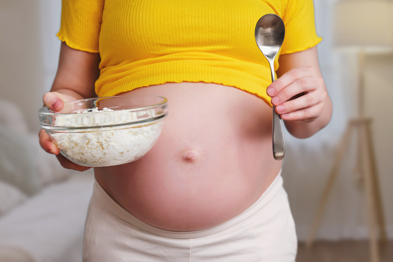A pregnant woman holding a bowl of cottage cheese.
