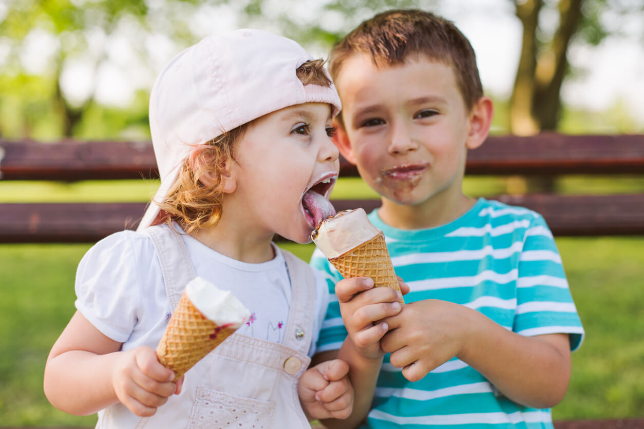 A little boy letting a little girl lick his ice cream cone.