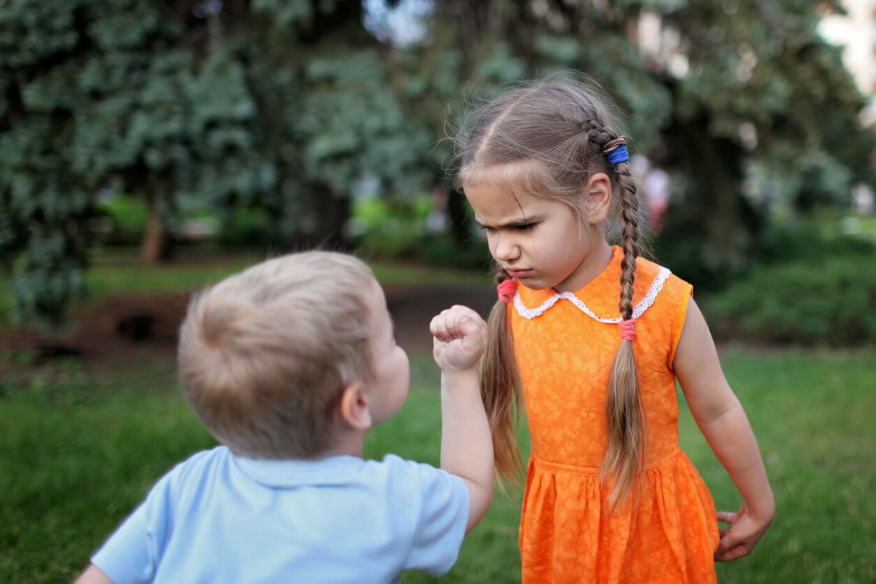 A young boy holding his fist up to his older sister, who's looking at him defiantly.