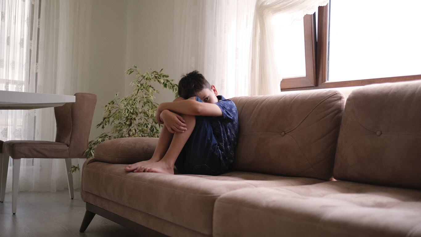 A sad child sitting curled up on a couch.