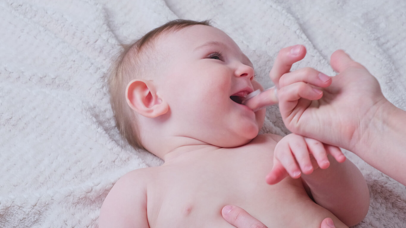 A woman using a finger brush to clean her baby's mouth.