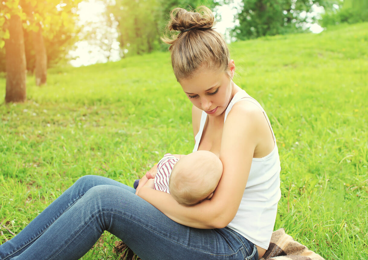 A woman nursing her baby while sitting in the grass.