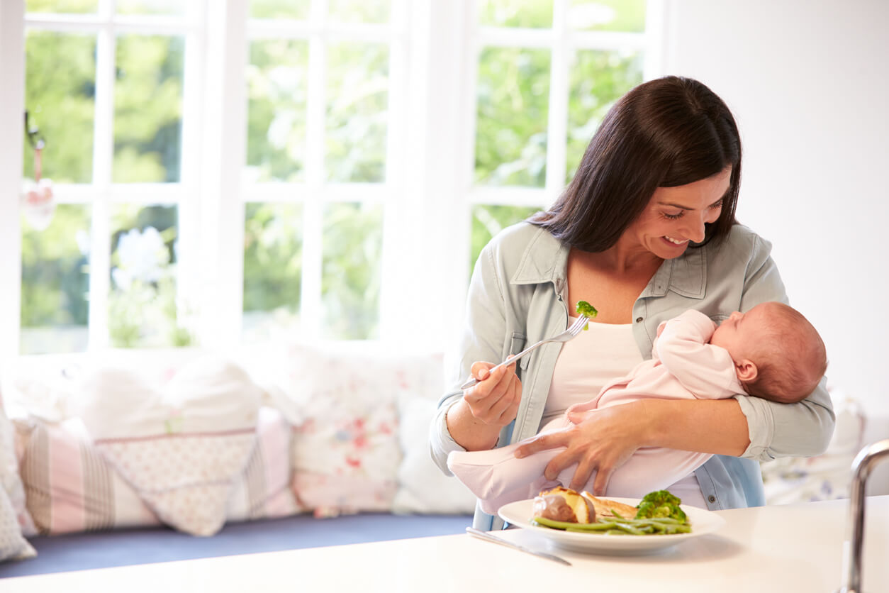 Une femme qui mange avec son bébé dans les bras. 