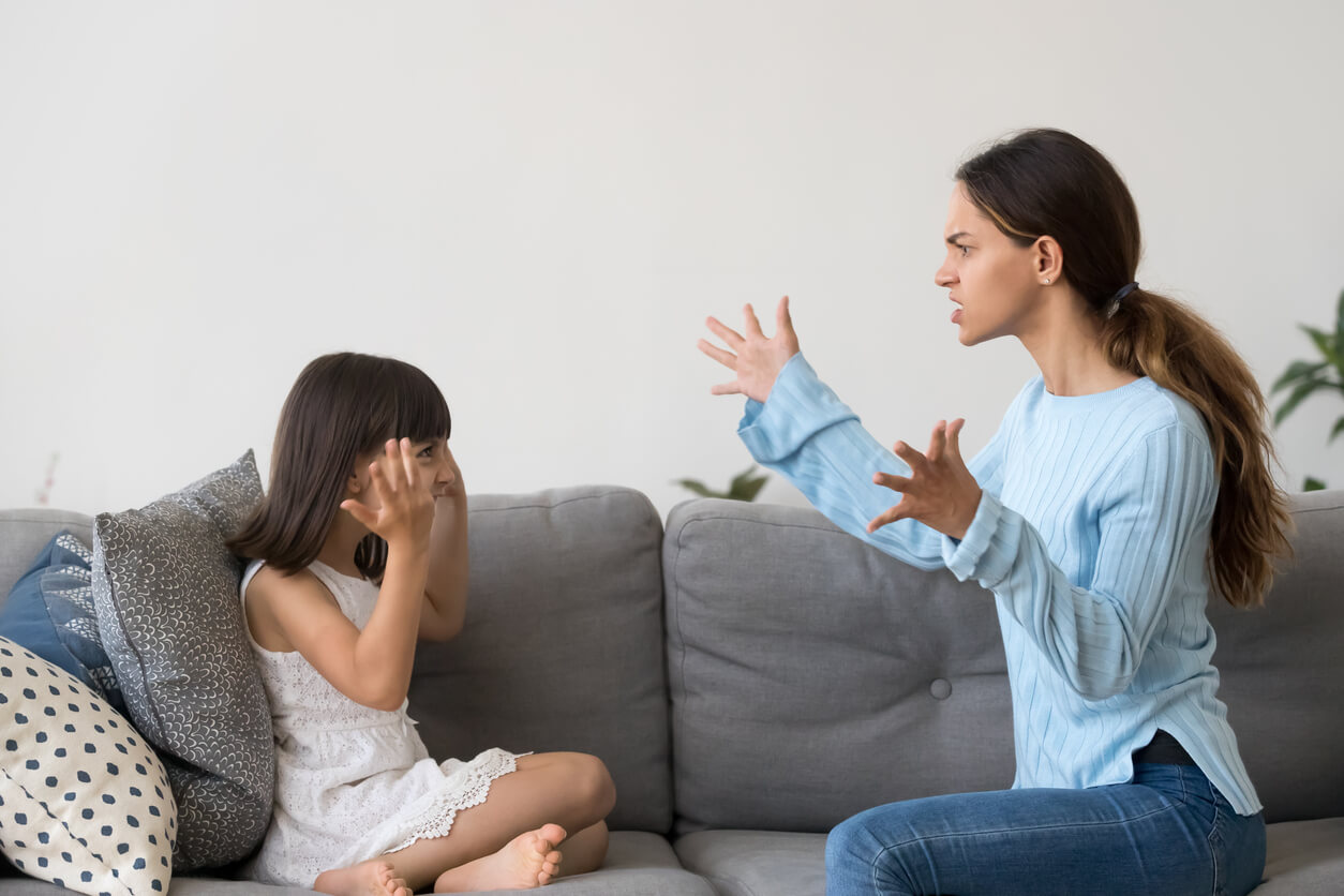A mother and her young daughter sitting on the couch, arguing.
