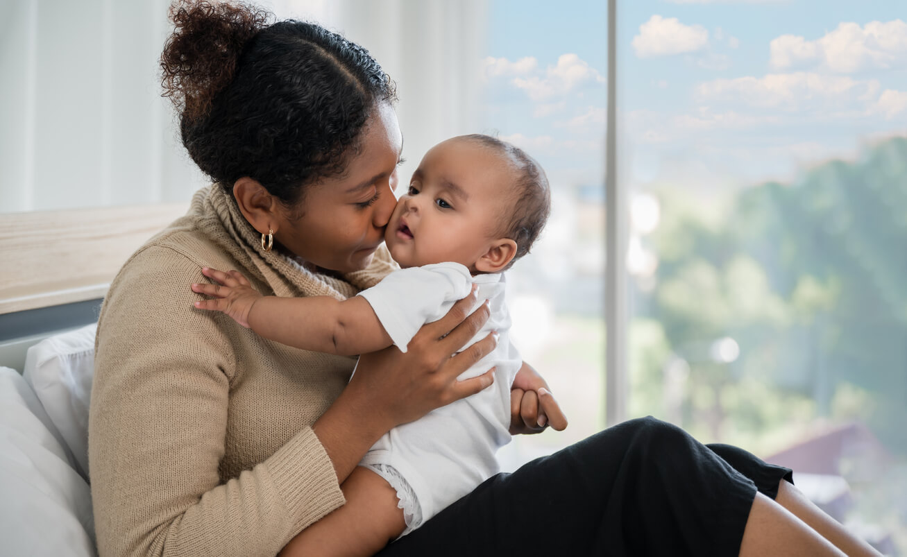 A black mother nuzzling her baby's cheek with her nose.