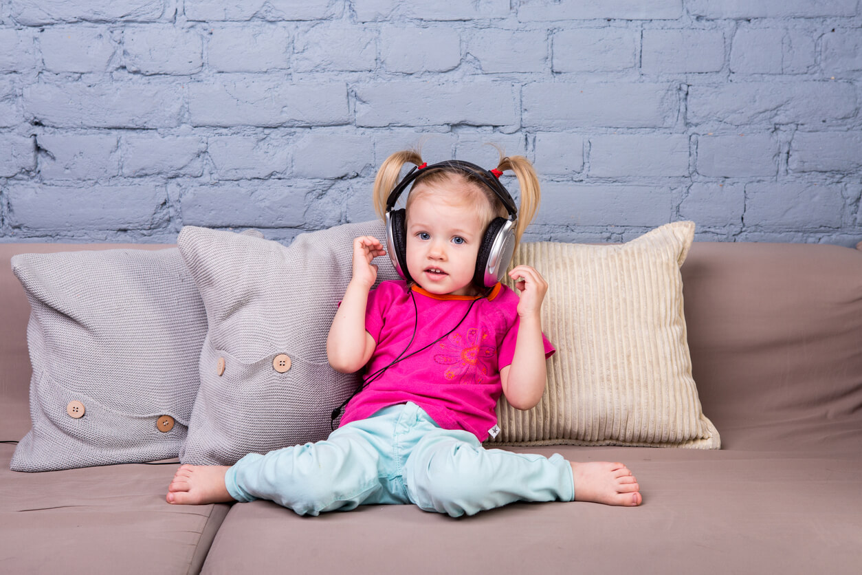 A toddler firl listening to music on headphones.