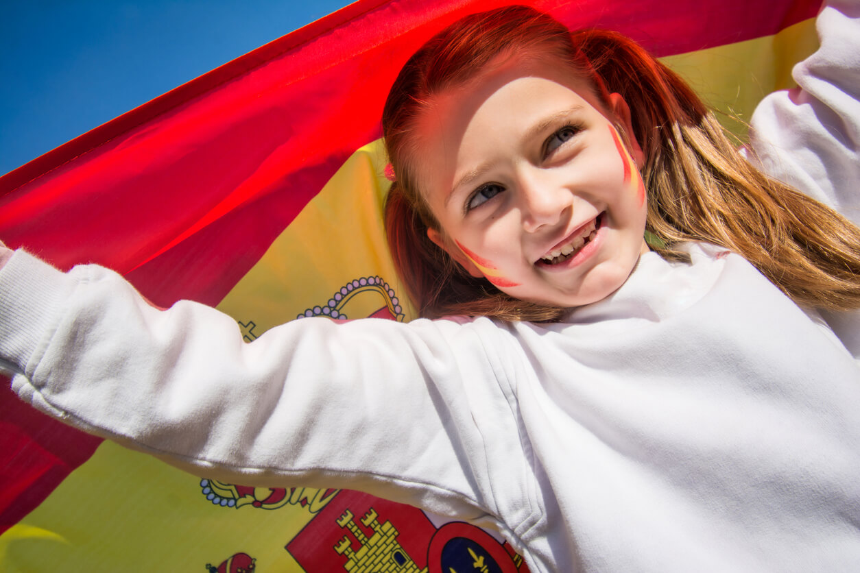 Une jeune fille qui étend le drapeau espagnol avec ses mains.