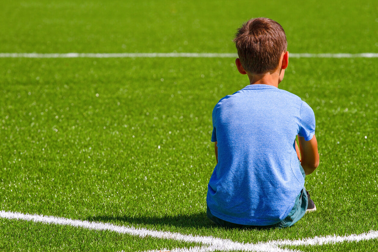 A child sitting on a soccer field with his bac turned toward the camera.