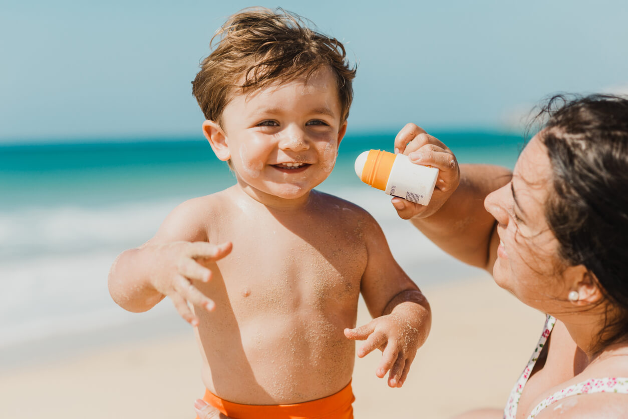 A mother putting sunscreen on her baby's skin at the beach.