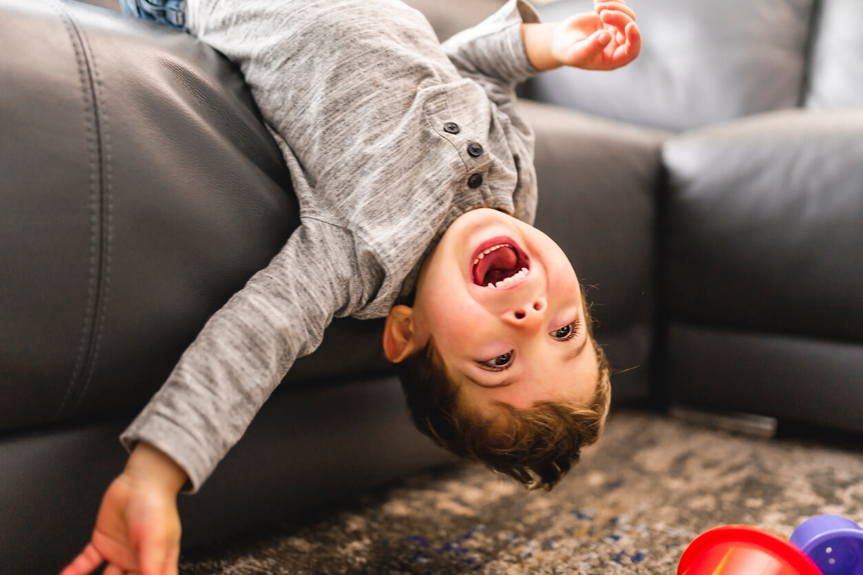 A child lying backward off a couch and laughing.