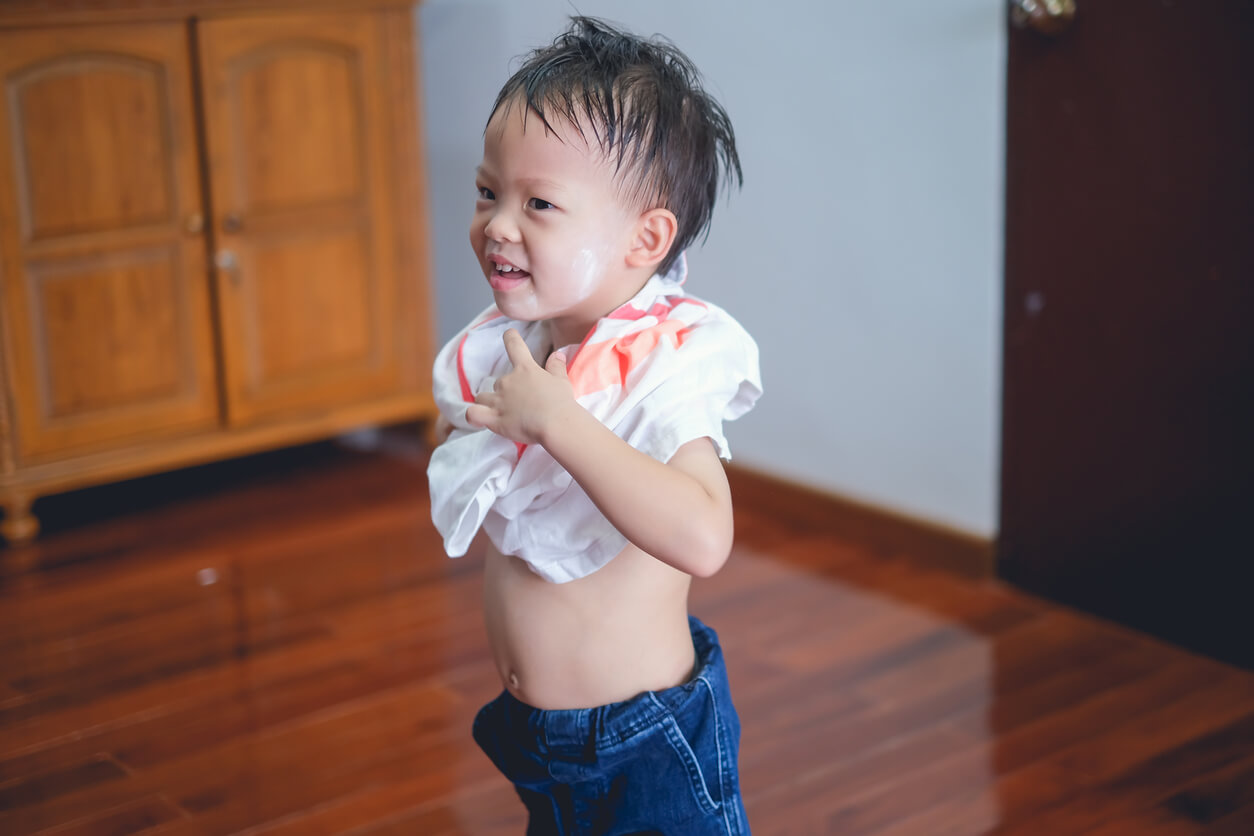 An Asian toddler getting dressed by himself.