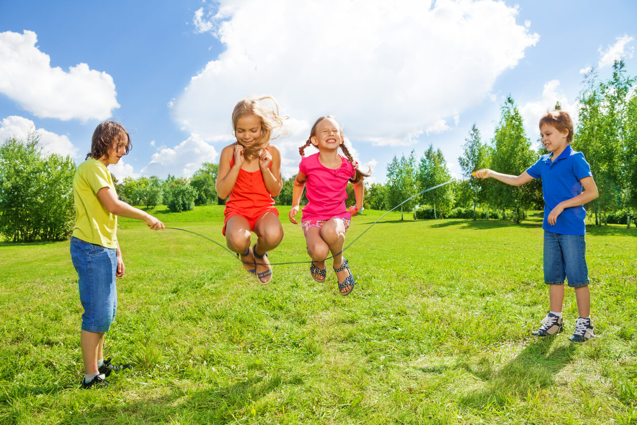 Four children jumping rope in a field.