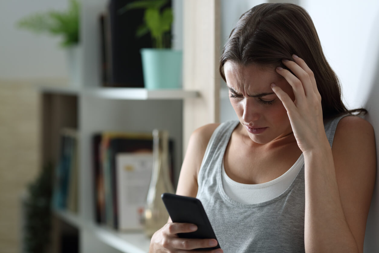 A teenage girl looking at her phone, upset.