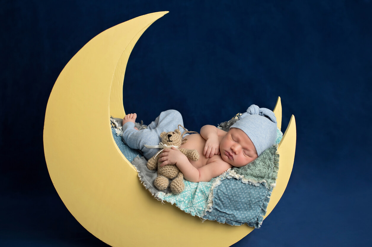 A photograph of a newborn baby sleeping in a moon-shaped cradle.