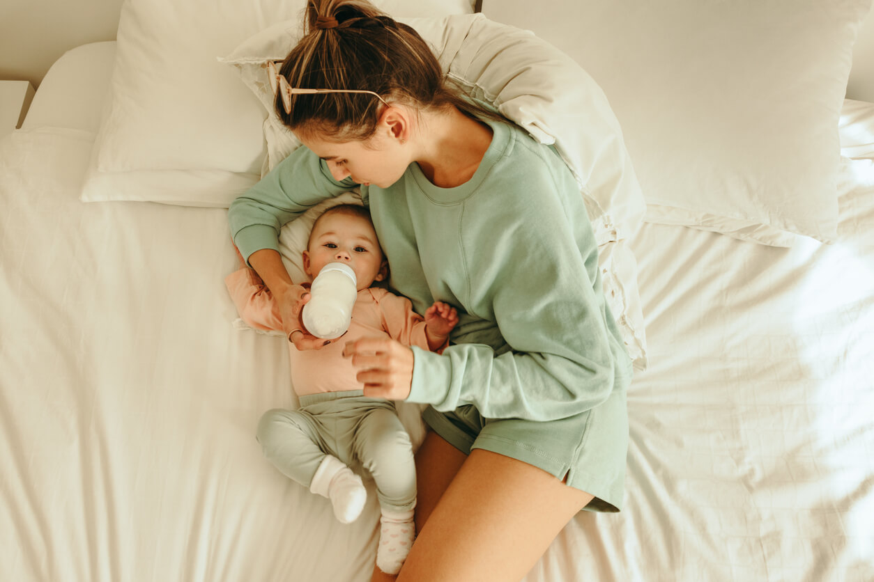 A mother bottle-feeding her baby in bed.