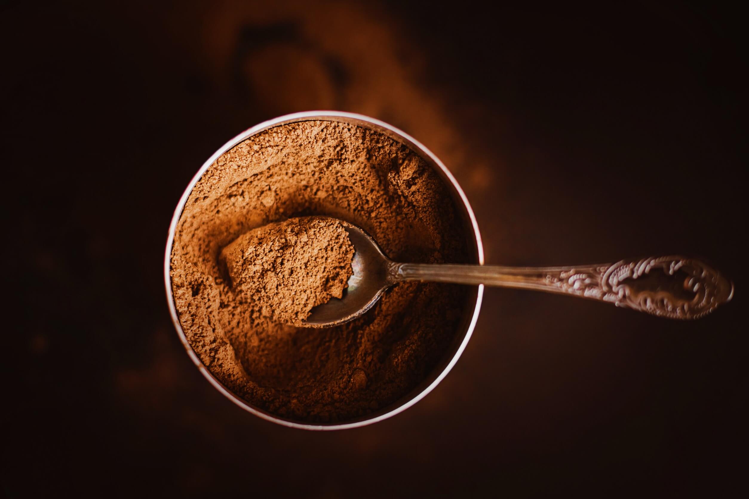 A siver spoon dipping into a metal canister full of cinnamon.