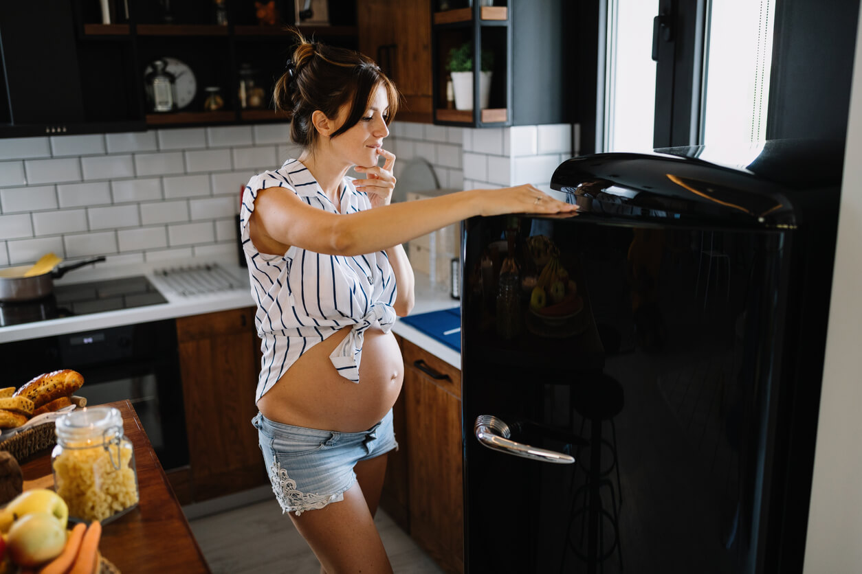 Une femme enceinte devant un frigo.