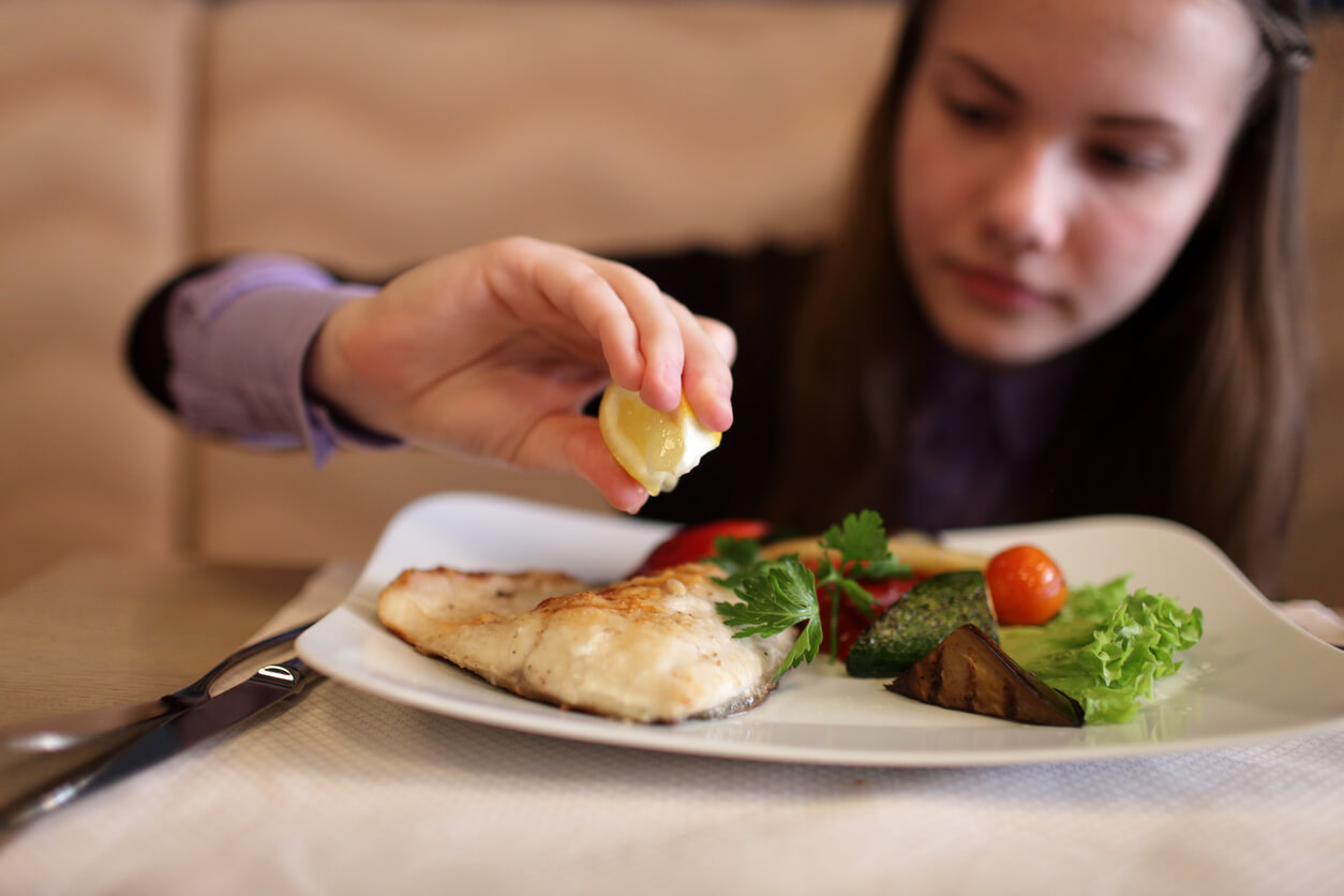 A young girl eating a healthy plate of fish and vegetables.