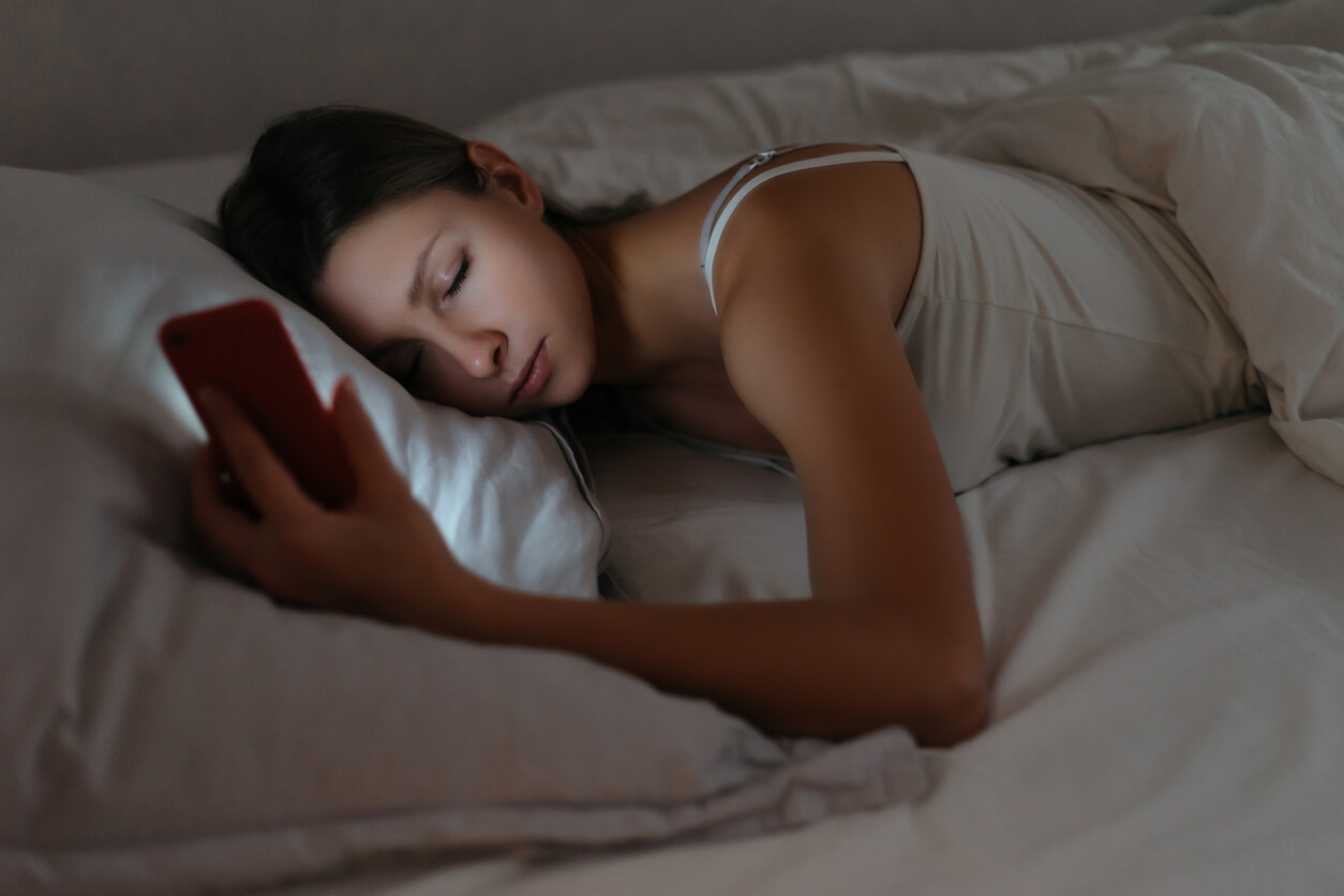 En tonårsflicka som sover med sin mobiltelefon i handen och lyser i ansiktet.