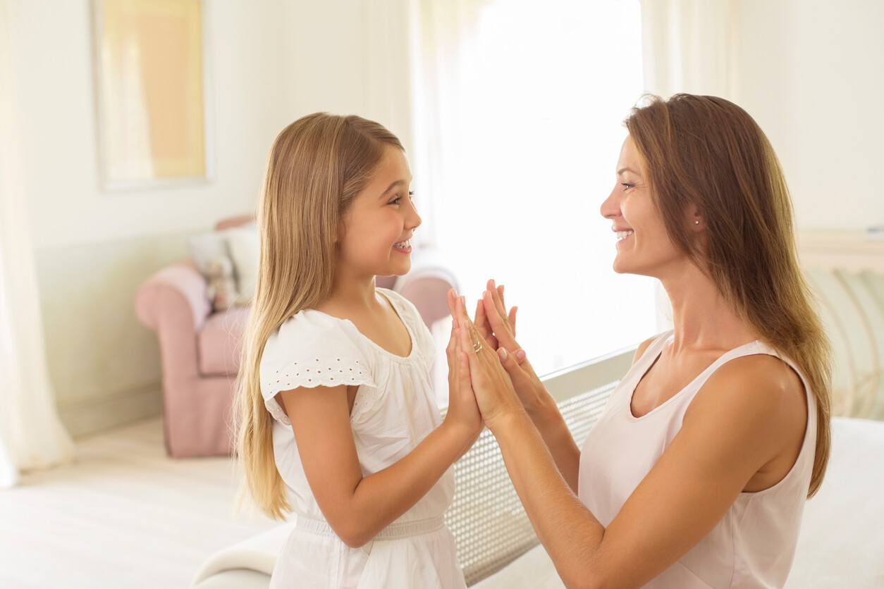 A mother and her daughter looking one another in the eye, smiling, and touching hands.