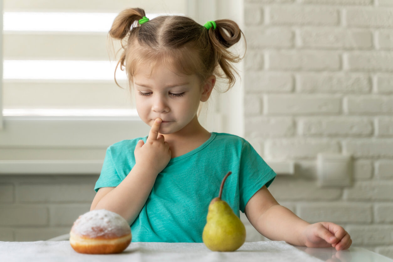 En liten jente tenker mens hun ser på et bakverk og en pære.