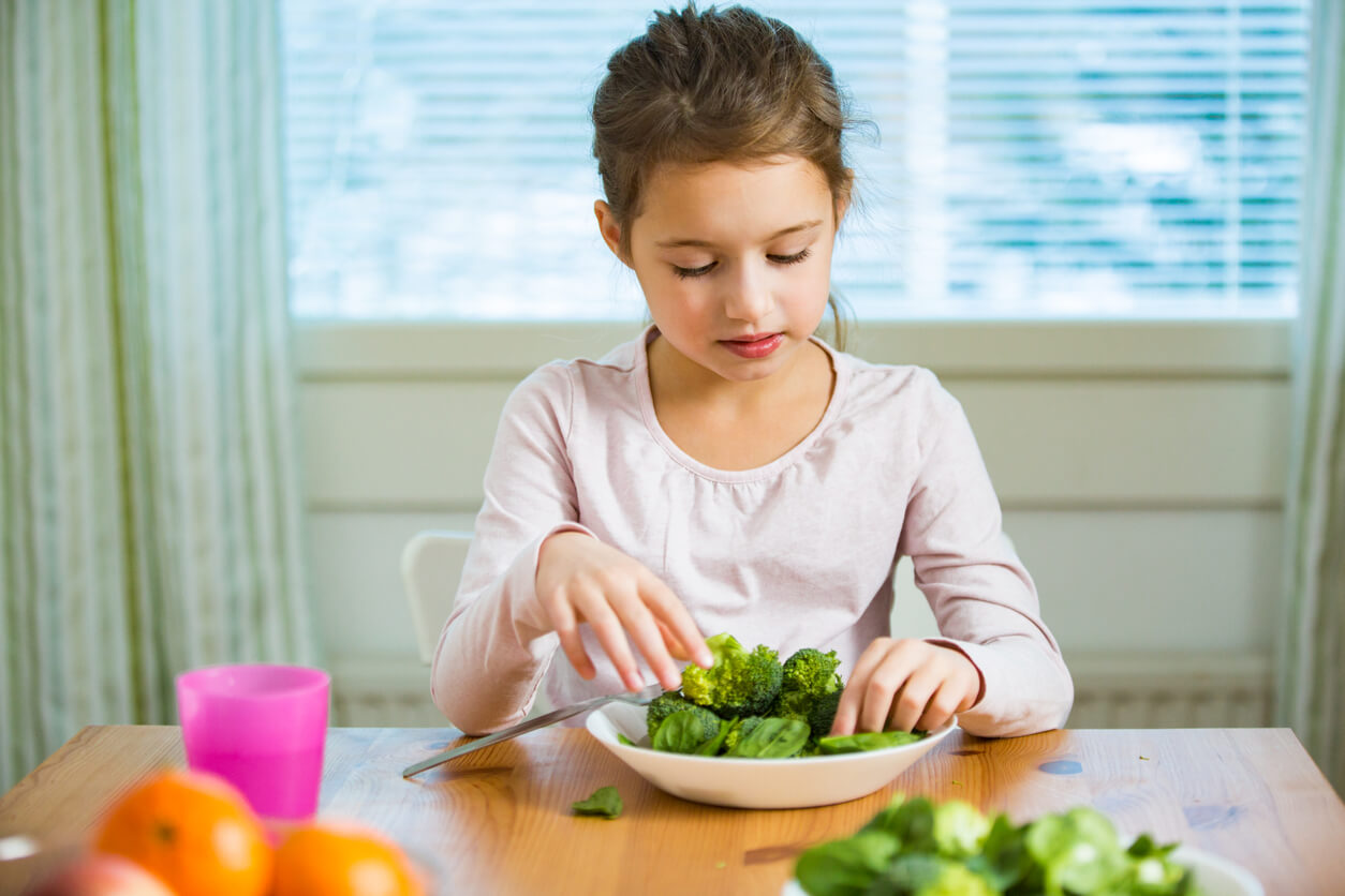 A young girl eating broccoli and spinach.