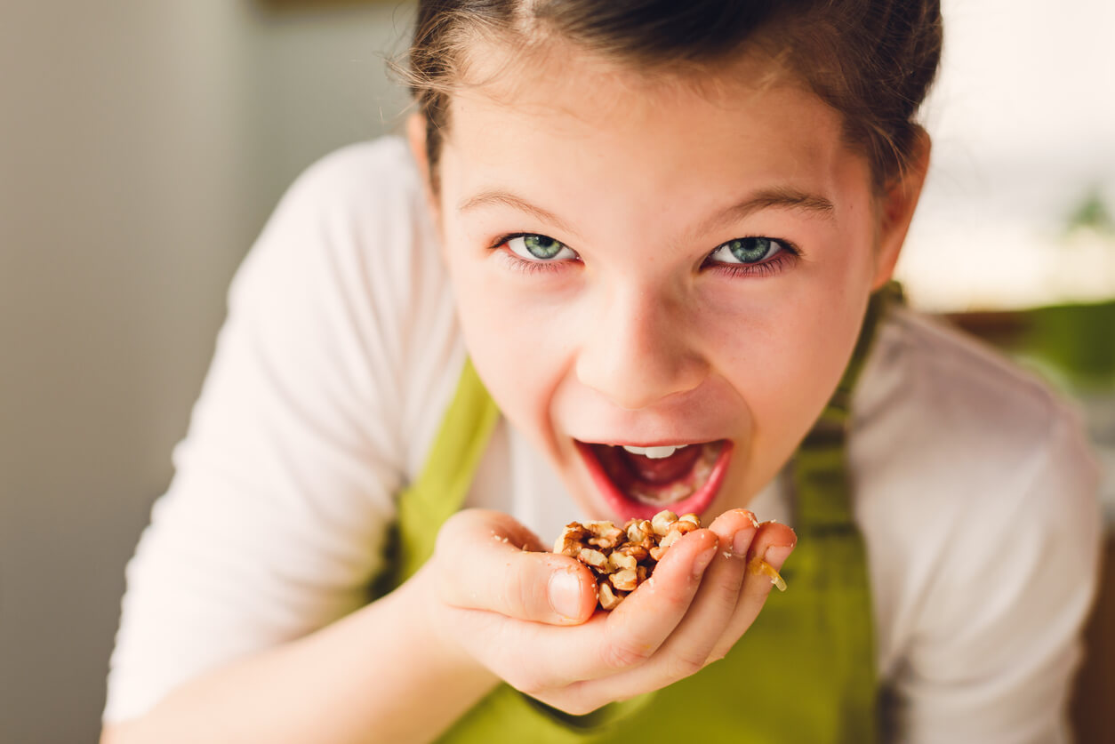 A young girl eating a handful of walnuts.