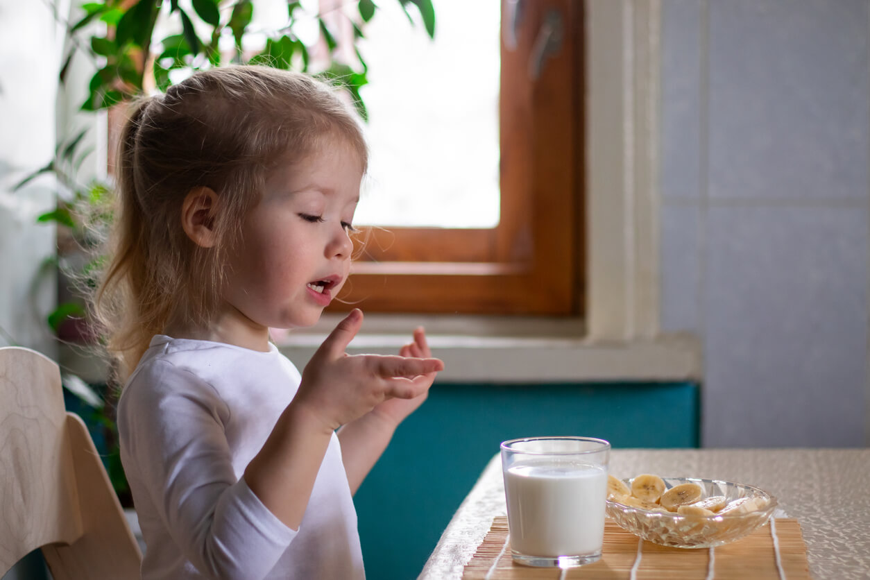 A little girl eating banana and drinking milk.