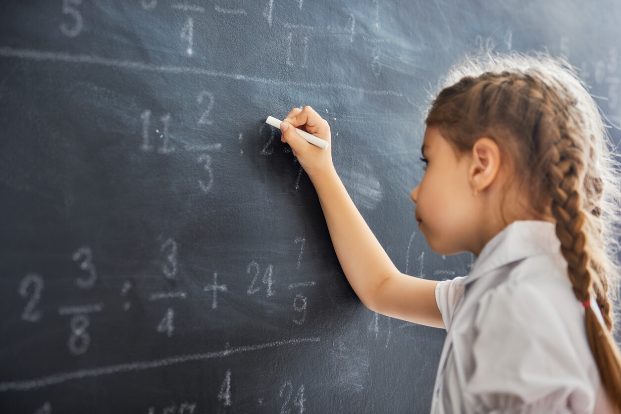A young girl doing math on a blackboard.