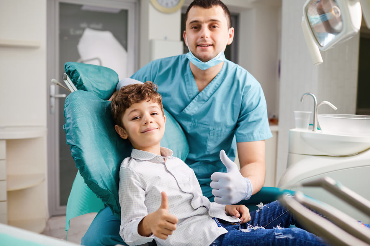 A dentist and a young male patient smiling and giving thumbs up.