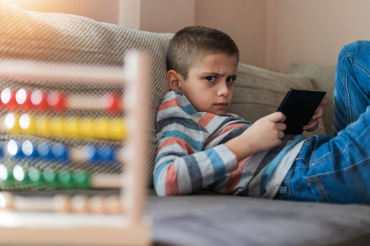 An angry child lying on the floor, looking at a tablet.