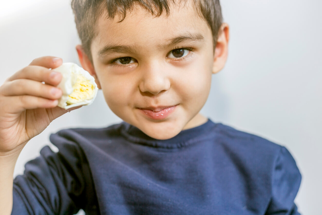 A preschool-aged boy eating a hard-boiled egg.