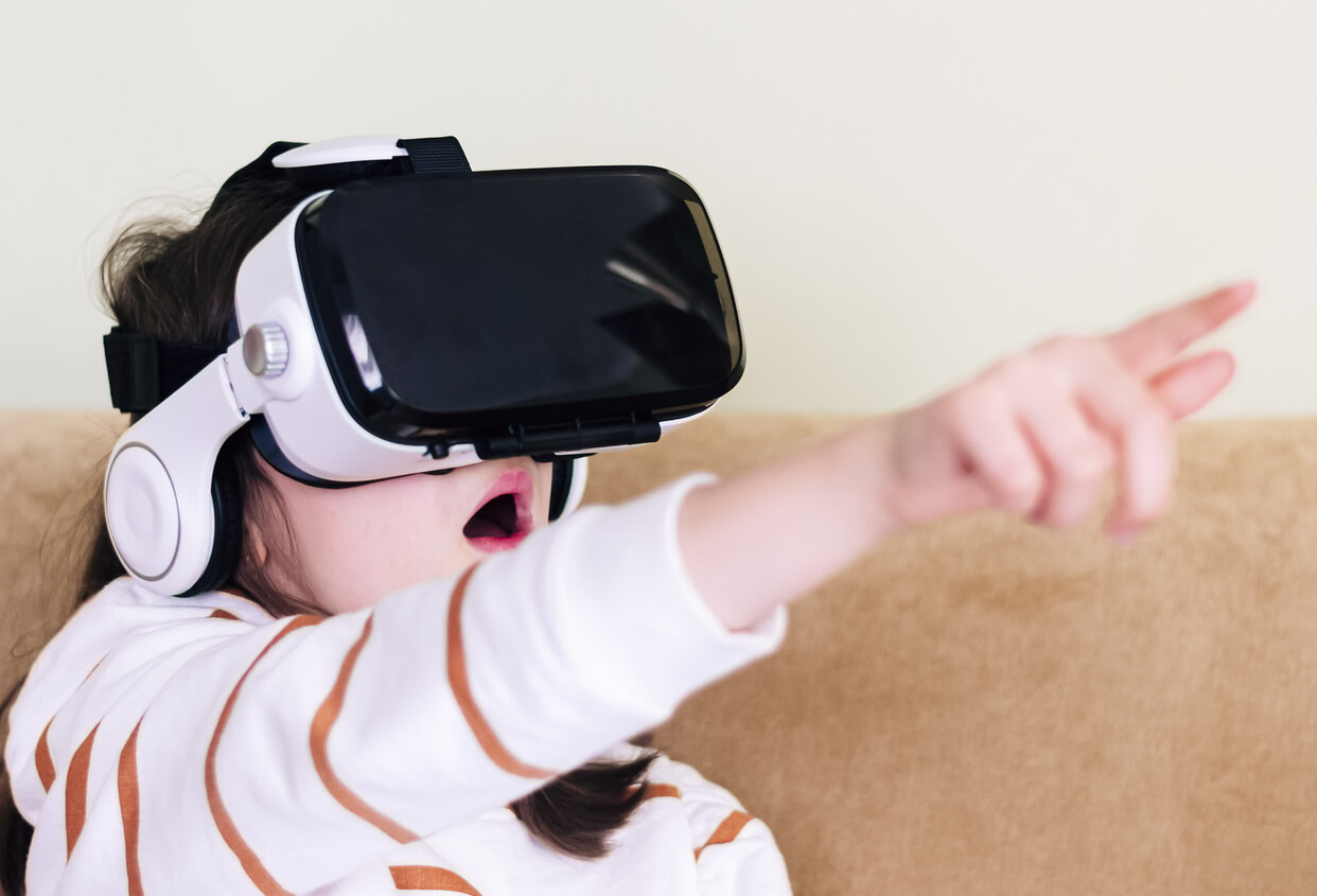A young girl pointing to an object while using a virtual reality headset.