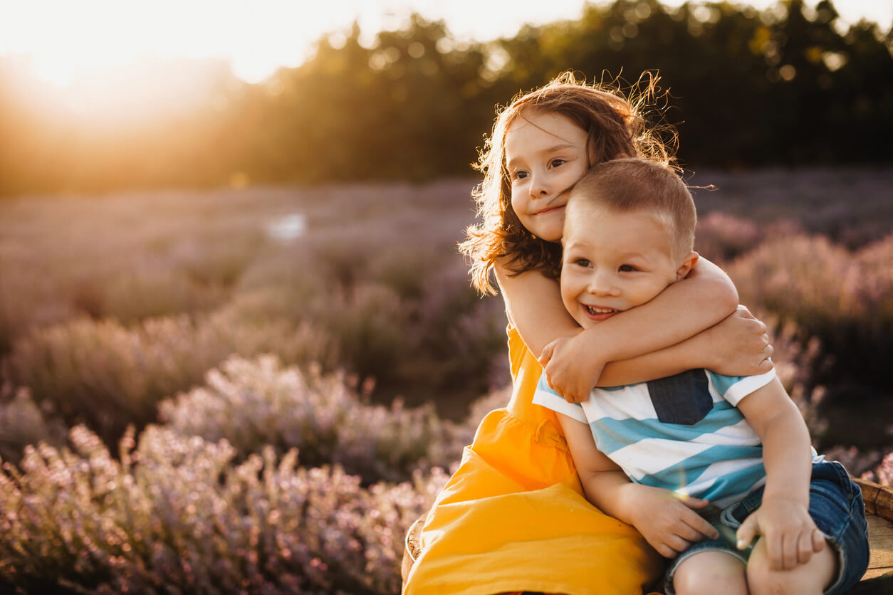 A little girl hugging her little brother in a field at sunset.