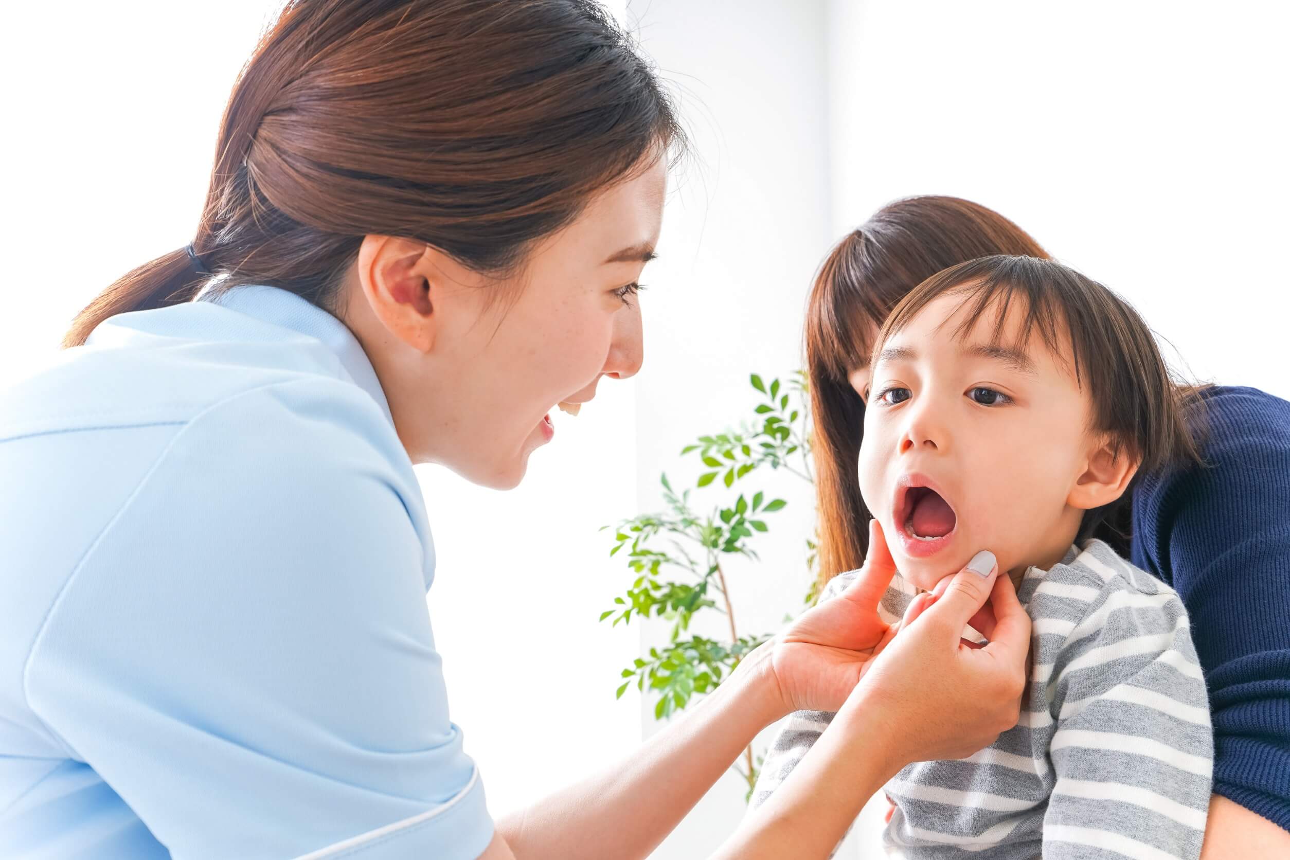 An Asian dentist examining an Asian boy's mouth while he sits on his Asian mother's lap.