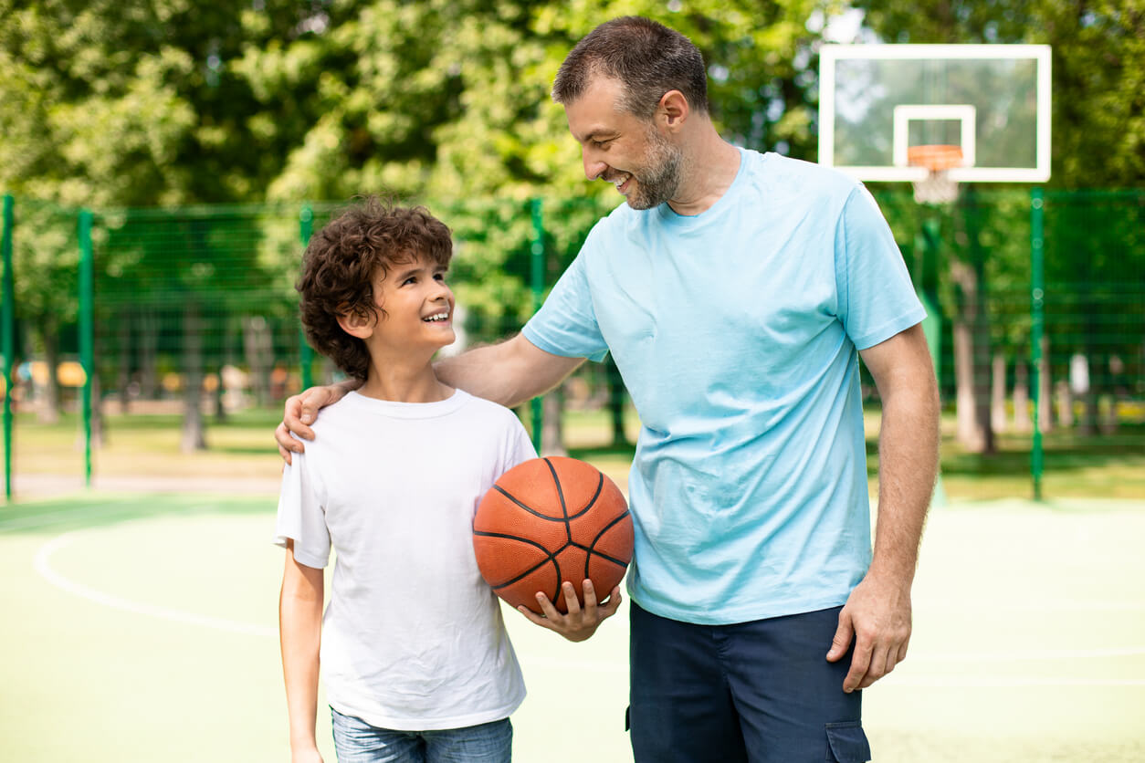 A father and son smiling at one another on a basketball court.