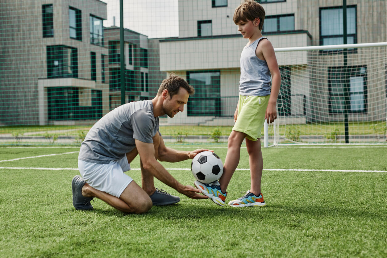 A father helping his son learn to play soccer.
