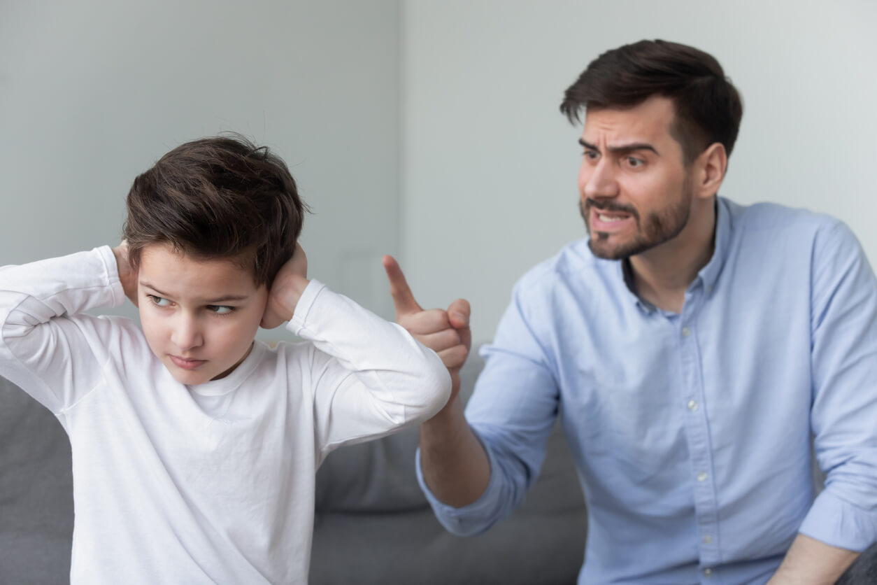 A young boy plugging his ears while his father yells at him.