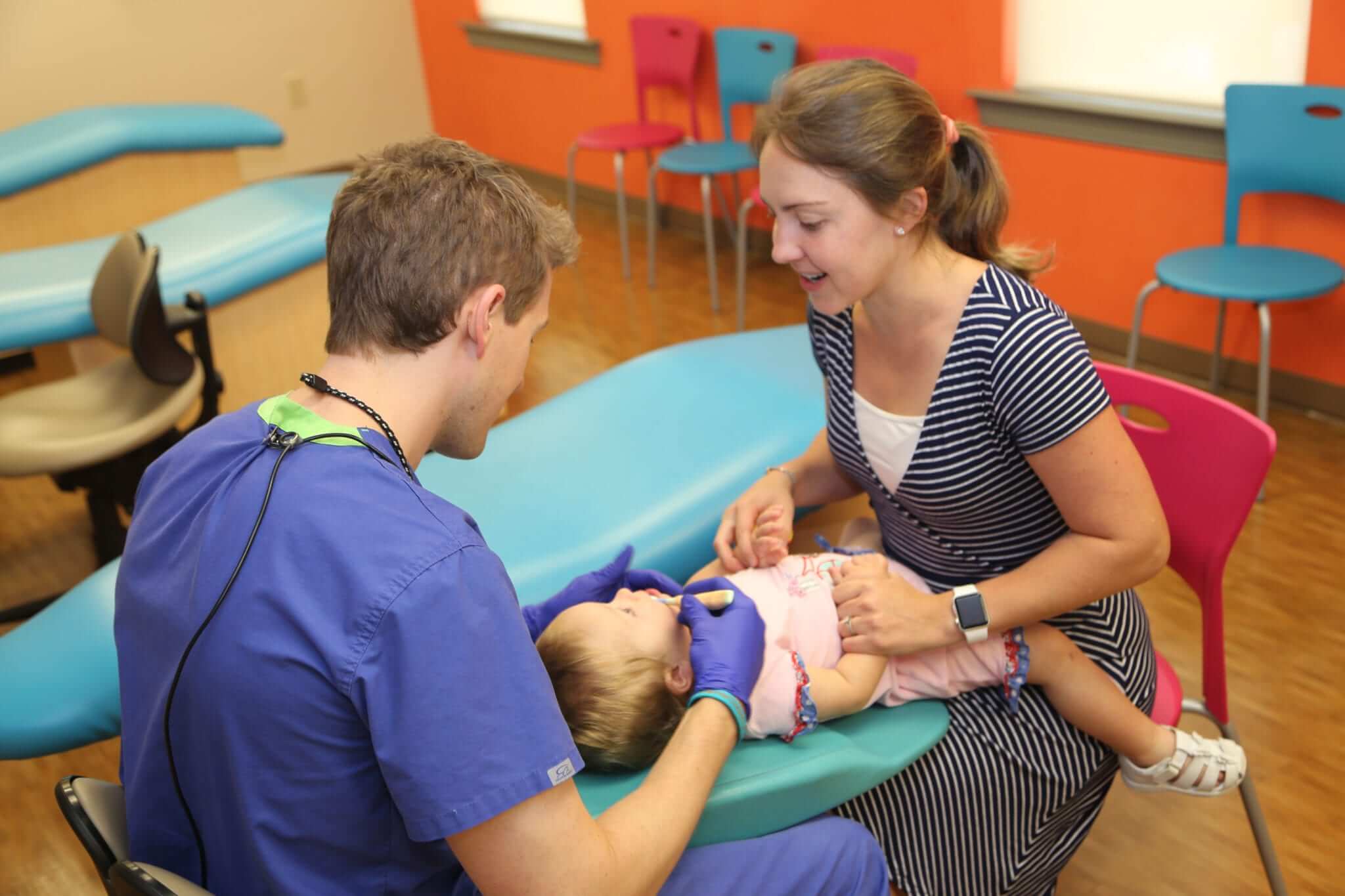 A dentist carrying out a knee-to-knee pediatric dental exam on a baby girl.