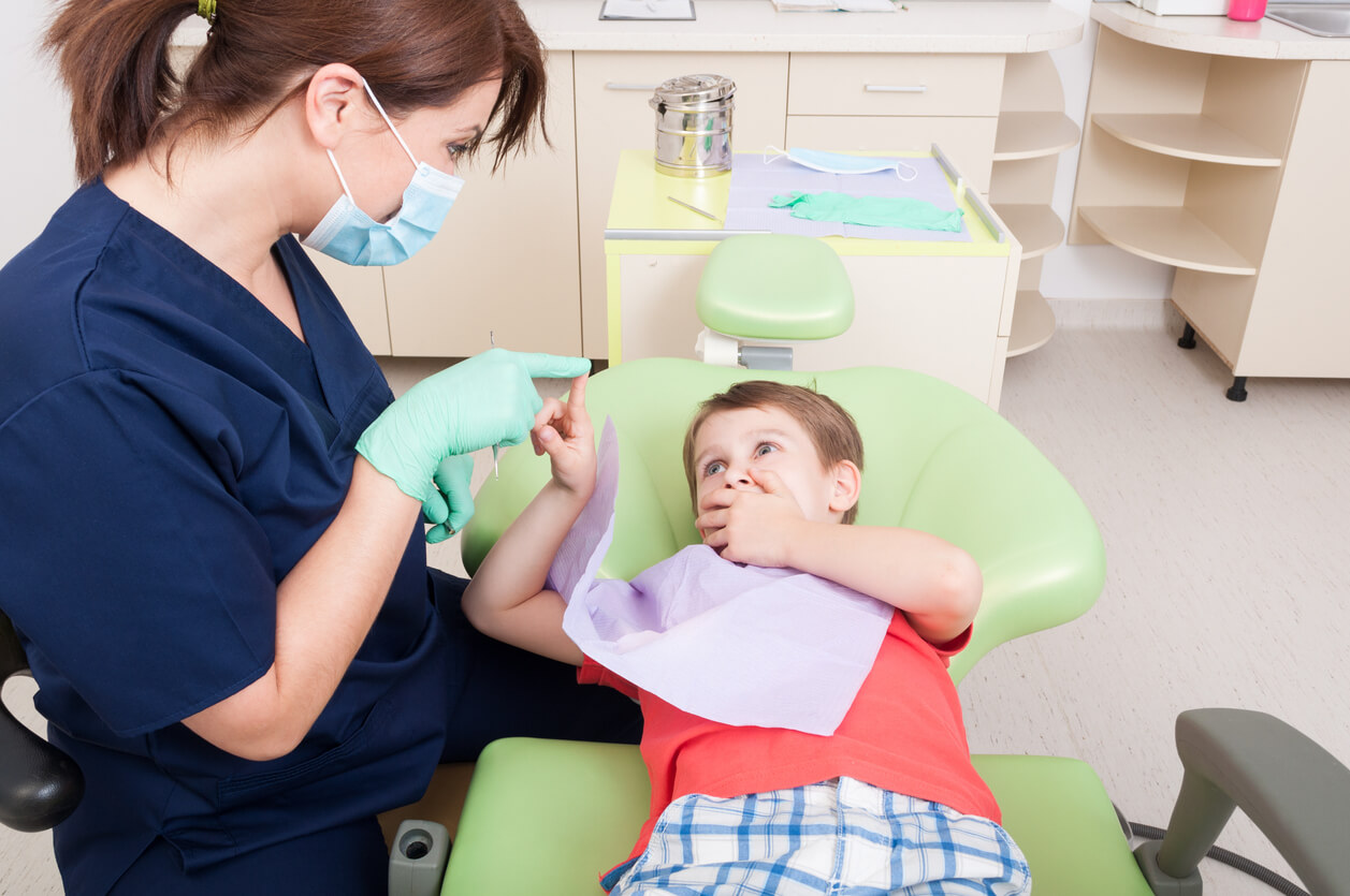 A young boy covering his mouth during a visit to the dentist.