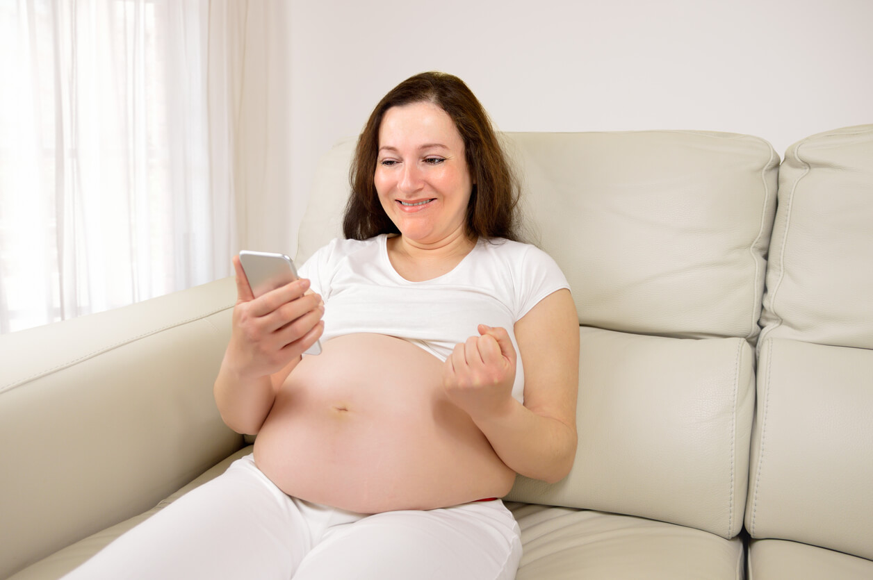 A pregnant woman looking at her cell phone and celebrating.