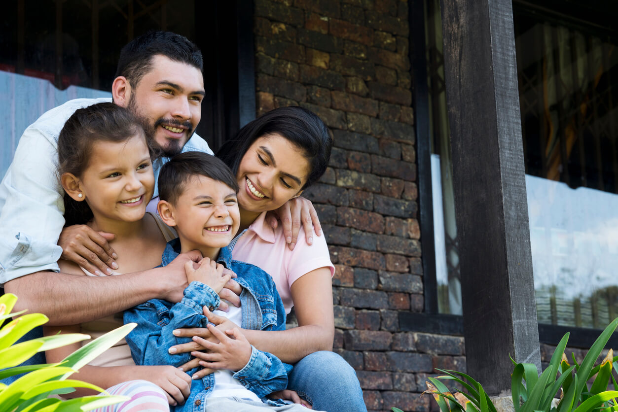 A Hispanic family sitting on the porch, positing for a family picture.