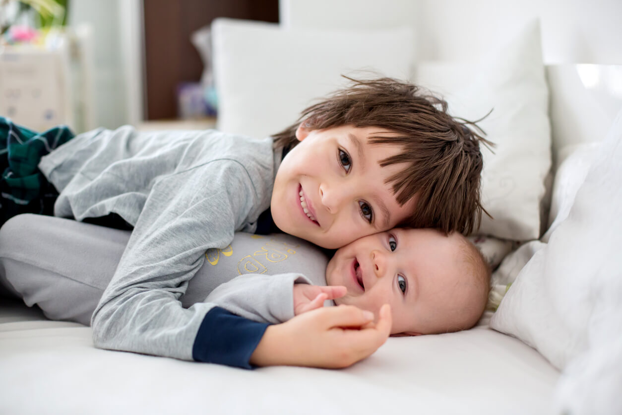 An older brother snuggling with his baby brother in bed.